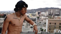 a shirtless man standing on a rooftop with a city view