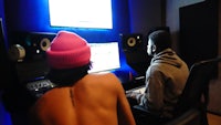 two people sitting in front of a monitor in a recording studio